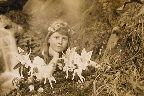 A photograph of Frances Griffiths posing with a group of fairies created from paper cutouts