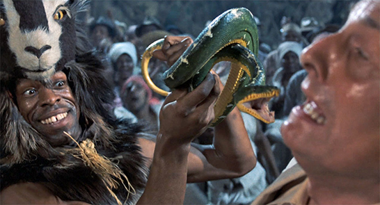 Witch doctor holds deadly snake near the face of a bound CIA agent